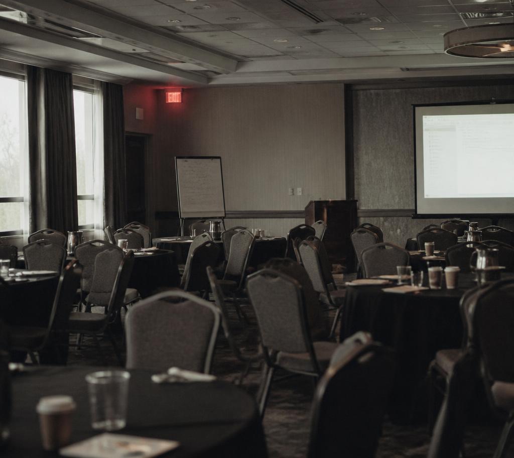 An empty hotel ballroom after a sales training workshop, chairs out of rows, a flip chart and a glowing projector screen in the afternoon light.